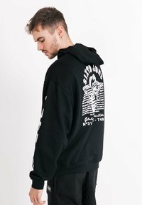 Schwarzer Sweatshirtpullover mit Kordelzug, der auf dem Rücken und an den Ärmeln weiße grafische Texte und Bilder zeigt, sowie gerippte Bündchen und Saum.