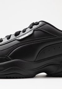 Sneaker noir Puma en cuir texturé, semelle épaisse, lacets noirs et logo Puma sur le côté près de la zone de lacets.