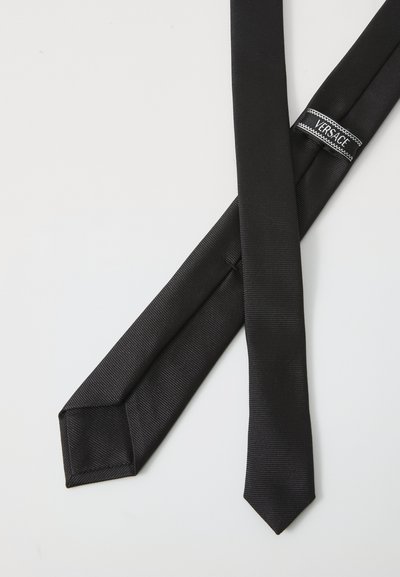 Cravate en soie noire avec une texture côtelée. Dotée d'une pointe pointue et d'une étiquette de logo Versace. Design plat, accessoire formel classique.