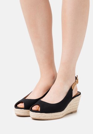 Sandalias de cuña de tela negra con diseño de punta descubierta, talón de cuña envuelto en yute y correa para el tobillo ajustable en un color marrón contrastante.