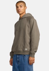 Oliwkowy hoodie wykonany z miękkiego materiału, z przednią kieszenią, regulowanym kapturem na sznurku oraz ściągaczami przy mankietach i u dołu.