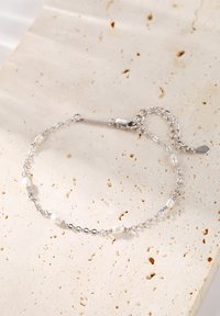 Bracelet en chaîne argentée ornée de perles de culture d'eau douce de forme irrégulière, avec un fermoir et une chaîne d'extension réglable. Fond texturé.