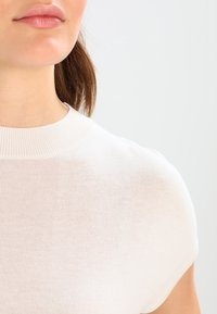 Svetle béžové tričko s krátkým rukávem a kulatým výstřihem, vyrobené z hladké, měkké látky. Má přiléhavý střih a jemnou strukturu.