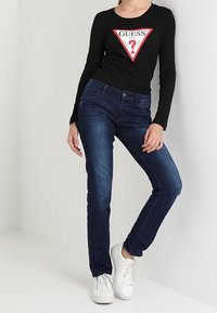 Zwarte lange mouwen top met een rood driehoeklogo; blauwe denim jeans; witte sneakers. Casual outfit met een getailleerd ontwerp en strakke lijnen.