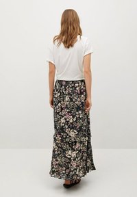 Jupe maxi florale en bleu marine foncé avec des fleurs violet clair et vertes, présentant un design à volants étagés. Complétée par un t-shirt blanc uni.