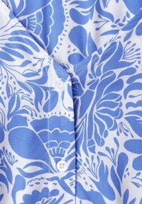 Tissu à motifs floraux bleu et blanc avec détail de couture boutonnée sur un matériau léger en coton.