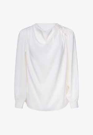 Witte blouse met lange mouwen, een geplooide halslijn en kleine bloemversieringen op één schouder, getoond tegen een effen achtergrond.