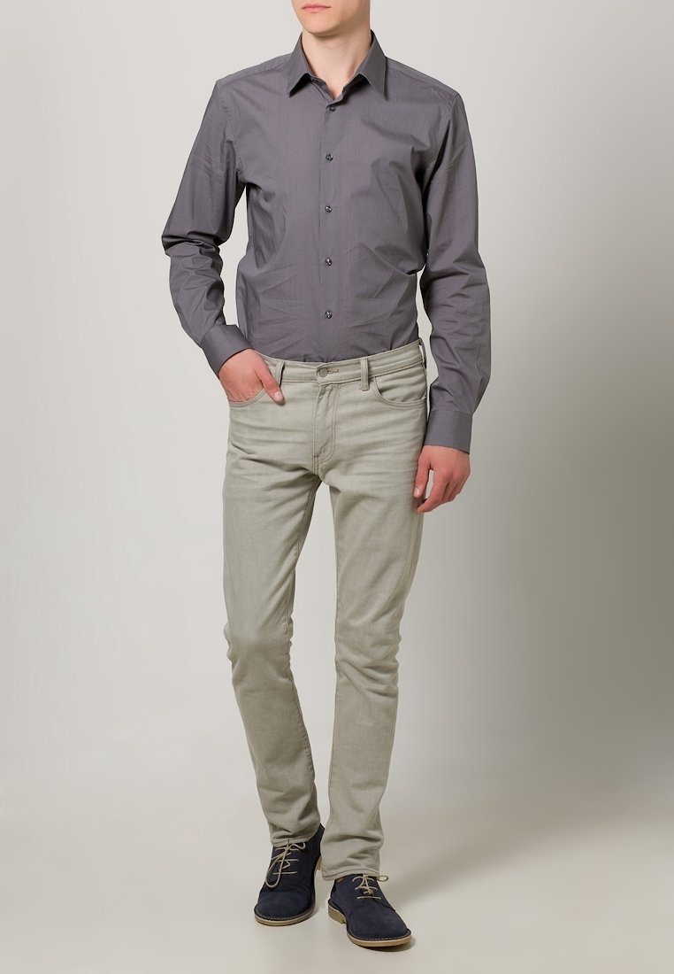 Chemise grise à boutons, jean beige et chaussures en daim bleu marine. Coupe slim, texture lisse et éléments de design subtils comme des boutons contrastants.