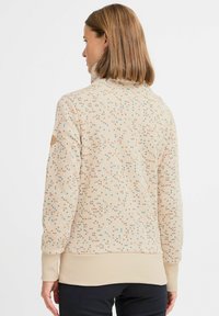 Felpa beige con un motivo a pois pastello, polsini e orlo a costine, colletto alto e dettagli del logo discreti sulla manica.