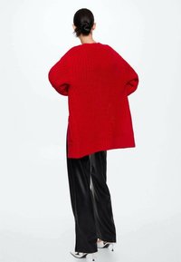 Punainen, ylisuuri neulepaita, jossa on paksu rakenne. Paidassa on roikkuvat olkaimet ja rento istuvuus, joka on yhdistetty mustiin leveälanteisiin housuihin.