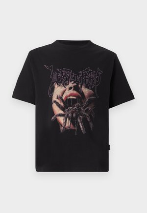 Μαύρο μπλουζάκι με γραφικό ενός ανοικτού στόματος και μια μεγάλη αράχνη που σέρνεται πάνω από τα χείλη και το πρόσωπο, με κείμενο από πάνω με στυλιζαρισμένα γράμματα.