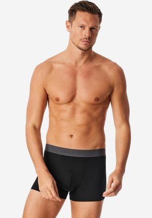 Musta puuvillaiset bokserishortsit, joissa on harmaa joustava vyötärönauha, jossa on "Schiesser"-logo. Istuvuus on vartalonmyötäinen ja materiaali sileä.