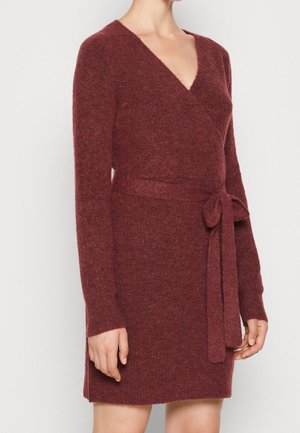 Langærmet, mørkerød strikket slå-om-kjole med V-udskæring og bundet taljebælte, båret af en person foran en ensfarvet baggrund.