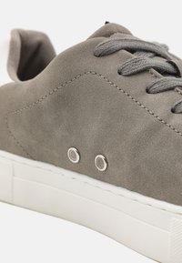 Gray suede sneaker with a rounded toe, gray laces, and silver eyelets. Features a white rubber sole and subtle texture.