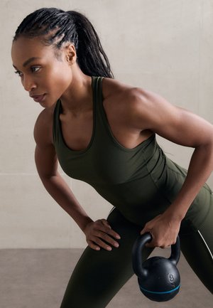 Must küllastunud must kettlebell sinise aktsendiga hoiab sportlikus tumeroheline särk ja vastavate legging'ide kandja, näidates lihaste määratlemist.