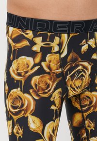 Black athletic leggings featuring a gold rose print, made from a stretchy material with a fitted design and branded waistband.