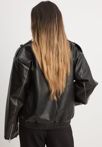 Giubbotto in ecopelle nera con vestibilità comoda, spalle basse, orlo a costine e dettagli in zip argentati sulle maniche.