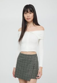Biała prążkowana bluzka crop top z dekoltem off-shoulder i zamkiem z przodu, zestawiona z wysokim, w kratkę mini spódnicą w odcieniach szarości i czerni.