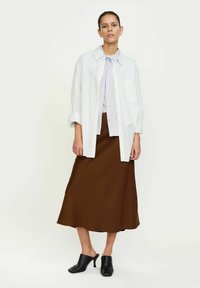 Csíkos fehér és világoskék ing, egy egyszínű levendula blúzra rétegezve, barna midi szoknyával és fekete magassarkú mules papuccsal párosítva.