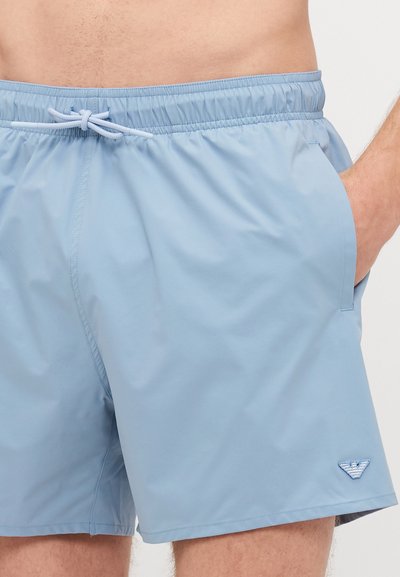 Shorts de bain bleu clair en matériau lisse et léger ; se caractérisent par une taille élastique avec cordon de serrage et des poches latérales.