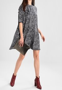 Mustat ja valkoiset kirjavakuosiset mekko lyhyillä hihoilla, löysä malli, polven ylle ulottuva pituus. Yhdistetty viininpunaisiin nilkkureihin ja mustaan clutch-laukkuun.