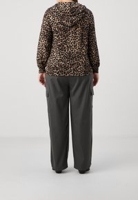Felpa con cappuccio in stampa leopardata beige e nera, abbinata a pantaloni cargo grigi a fantasia larga con tasche laterali. Texture di tessuto morbido.