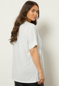 Hvid kortærmet t-shirt med oprullede ærmer, lavet af letvægtsstof, med en løs pasform og sideslids for komfort.