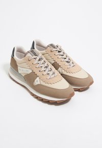 Beige en lichtbruine sport schoenen met een leren bovenlaag, zigzagranddetails, platte veters en een rubberen zool met een grijze hakaccent.