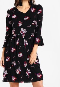 Svart klänning med trekvartslånga trumpetärmar med ett blommönster i nyanser av röd, vit och blå. V-ringad design och utställd fåll.