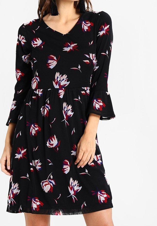 Svart klänning med trekvartslånga trumpetärmar med ett blommönster i nyanser av röd, vit och blå. V-ringad design och utställd fåll.