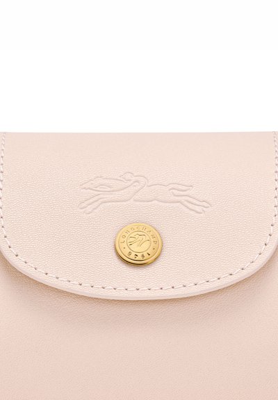 Close-up of pale pink leather flap with embossed running horse logo and round gold snap button engraved with "LONGCHAMP 1948."