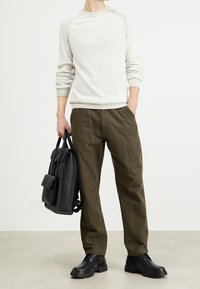 Kremowy sweter w prążki, spodnie w oliwkową kratę, czarne skórzane buty oraz czarny skórzany plecak z przednią kieszenią.