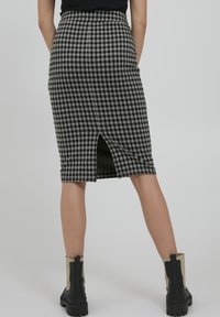 Jupe midi en vichy noir et blanc avec une fente au dos, présentant une silhouette ajustée et portée avec des bottines chunky noires et beiges.