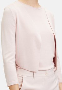 Světlý růžový kardigan s krátkým střihem, kulatým výstřihem a tříčtvrtečními rukávy, doplněný o sladěný světle růžový top a kalhoty.