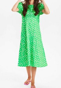 Zielona sukienka w kropki, z krótkimi bufkowymi rękawami, długości do kolan, wykonana z gładkiego materiału. Połączona z różowymi sandałami.