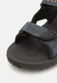 Mustad mustkatega sandaal tekstuuriga rihmaga ja pehme jalanõu sisemusega. Omab reguleeritavaid Velcro sulgureid ja mustrilist kummist välispinda.
