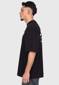 Black cotton t-shirt with short sleeves, relaxed fit, featuring a printed logo and horizontal stripes in red and white on the front.