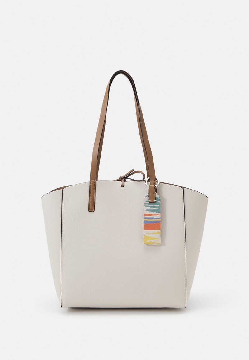 Sac cabas crème avec des poignées marron et un porte-clés rectangulaire multicolore suspendu à une poignée.