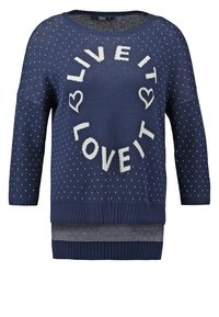 Mörkblå stickad tröja med vita prickar, med texten "LEVA DET ÄLSKA DET" och hjärtaccentuer. Ribbstickade muddar och nederkant.