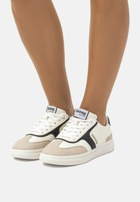 Sneakers bianchi e beige con accenti neri, dotati di una tomaia in pelle liscia, pannello in suede testurizzato e lacci tradizionali.