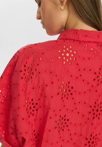 Blusa rossa ricamata con motivi a fiori ritagliati, tessuto leggero, trama a rete aperta e design rilassato senza colletto.