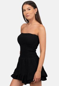 Zwarte straploze jurk met een gestructureerde stof, een nauwsluitende lijfje en een uitlopende rucheszoom. Gladde, lichte materialen.