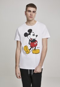 Balta medvilninė marškinėliai su dideliu Mickey Mouse grafikos atvaizdu, vilkintį raudonus šortus ir geltonus batus, apvali iškirptė, trumpomis rankovėmis, laisvas siluetas.