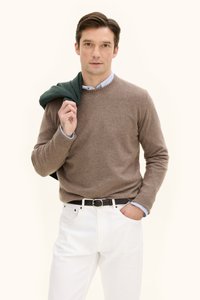 Ruskokoinen neulepusero vaaleansinisen kauluspaidan päällä, valkoiset housut ja musta vyö. Vihreä huivi on heitetty hänen olkapäänsä yli.