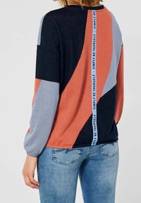 Färgglad tröja med blockmönster i marinblått, rostfärg och ljusblått, med en vertikal textdetalj längs ryggen i vitt.