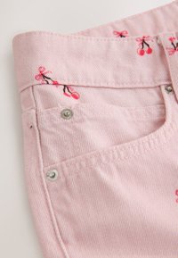 Gros plan sur un tissu en denim rose avec de petites impressions de cerises rouges et des rivets métalliques près des bords des poches.