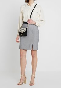 Vaaleanbeige pitkähihainen paita, harmaa polvipituinen kynähame, jossa on edessä halkio, pieni musta käsilaukku, jossa on käärmeennahkakuviollinen läppä, ja kultaiset korkokengät.