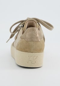 Beige Wildleder-Sneaker mit einer strukturierten cremigen Sohle, ausgestattet mit einem metallischen Akzent an der Ferse und flachen Schnürsenkeln. Logo auf der Sohle eingestanzt.