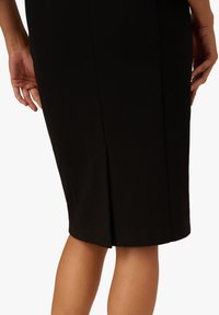 Jupe crayon noire en tissu texturé, avec une fente au dos. L'ourlet est droit et elle s'ajuste étroitement au corps.