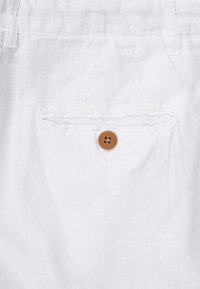 Bílé lněné šortky se přední kapsou a hnědým knoflíkem na zapínání, které se vyznačují hladkou texturou a lehkým designem.